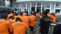 Polisi menggiring puluhan tersangka yang terjaring gerebekan dalam "LGBT Siwalan Party" menuju ke ruang tahanan di Polrestabes Surabaya, Rabu (22/10/2025). foto ant